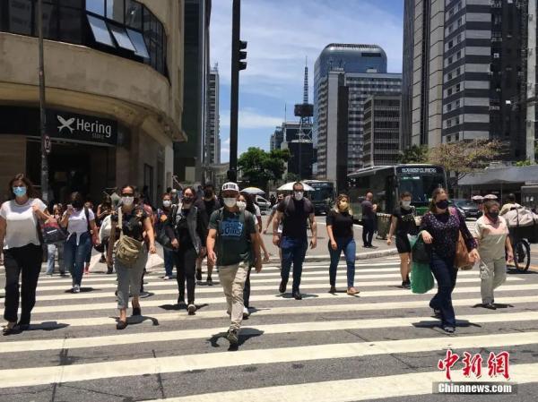 资料图。巴西圣保罗，戴口罩的民众横过马路。